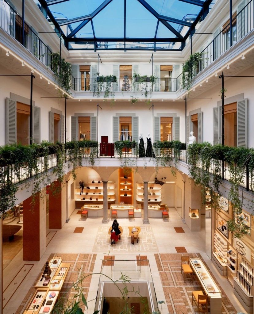 Interior view of the newly reopened Louis Vuitton store in Milan, showcasing a modern yet elegant design with a central atrium, glass roof, and lush greenery.