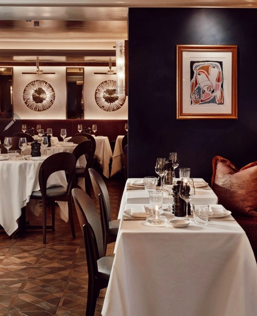 Interior view of Sale e Pepe restaurant featuring elegantly set tables with white tablecloths, dark wooden chairs, and sophisticated decor, including art on the walls and atmospheric lighting.