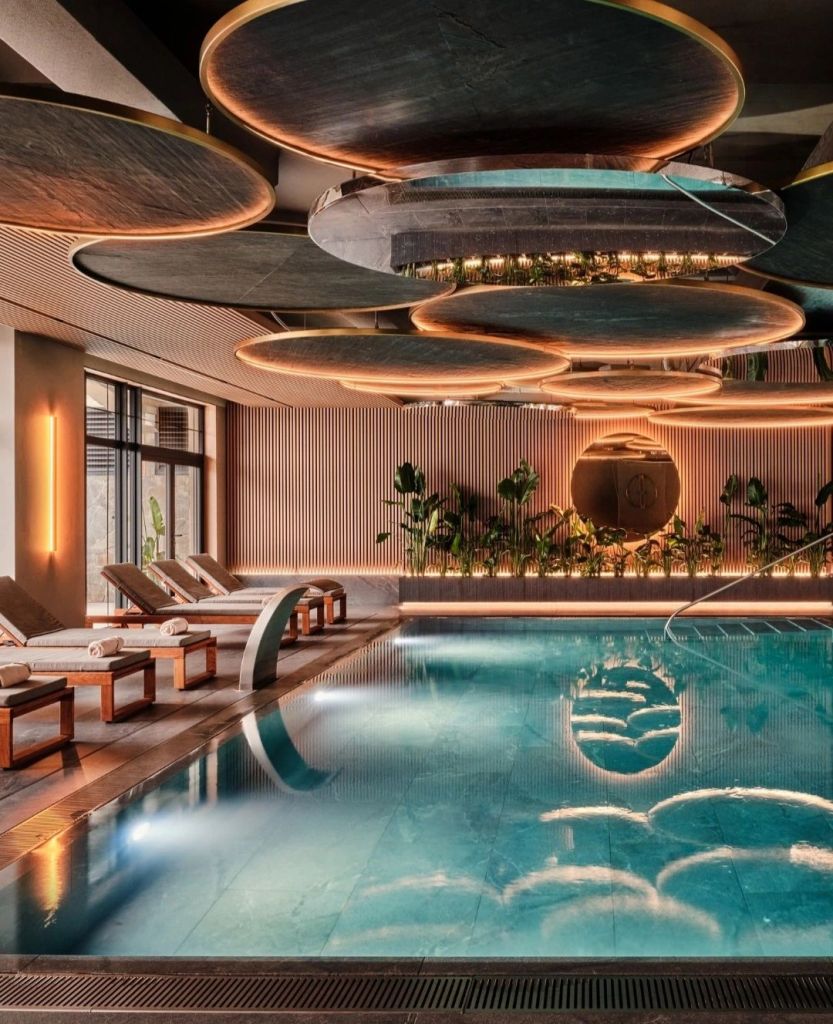 Interior view of a luxury hotel spa featuring a sleek swimming pool, elegant loungers, and modern lighting elements.