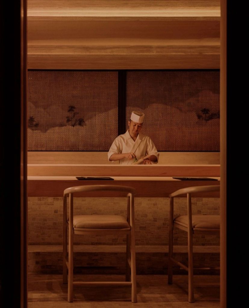 A chef preparing food at a minimalist wooden counter in a serene restaurant setting.
