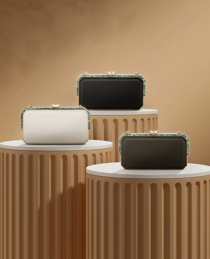 Three luxury handbags displayed on elegant pedestals, featuring a white, black, and dark green design with intricate detailing.