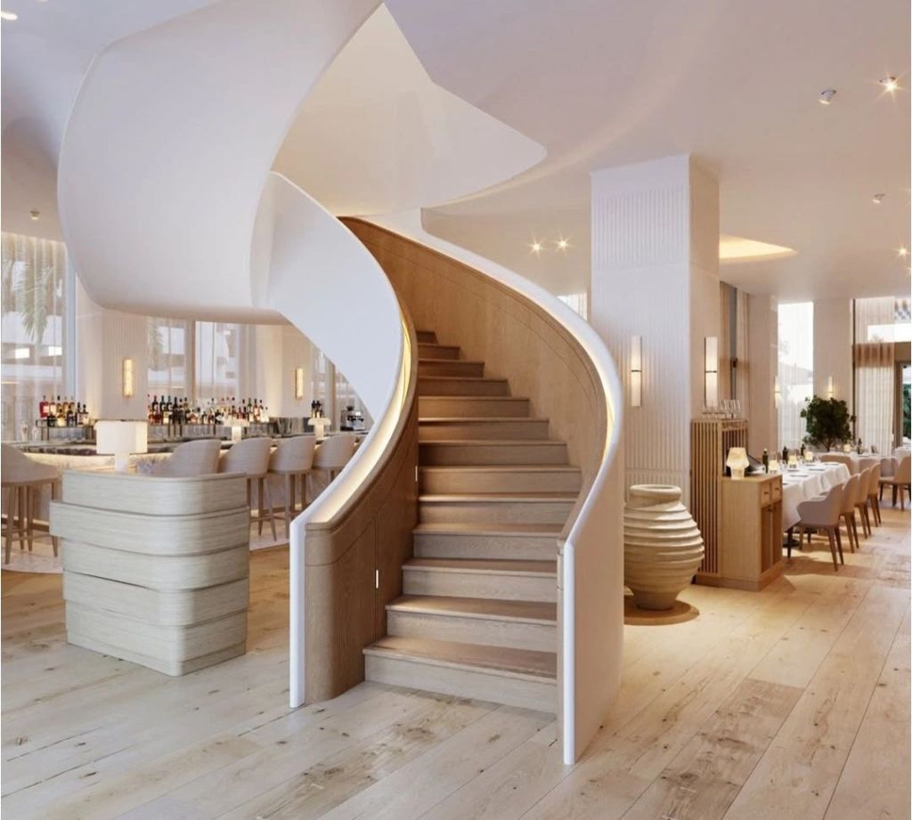 Elegant spiral staircase made of wood and stone, leading to an upscale dining area with a bar, showcasing modern interior design and warm lighting.