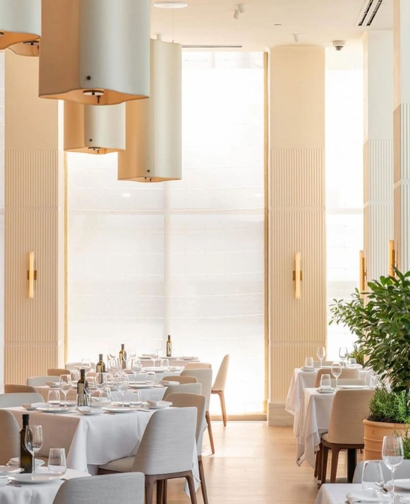 Interior view of the estiatorio Milos restaurant in West Palm Beach, showcasing elegant dining tables with white linens, stylish chairs, and soft lighting fixtures.