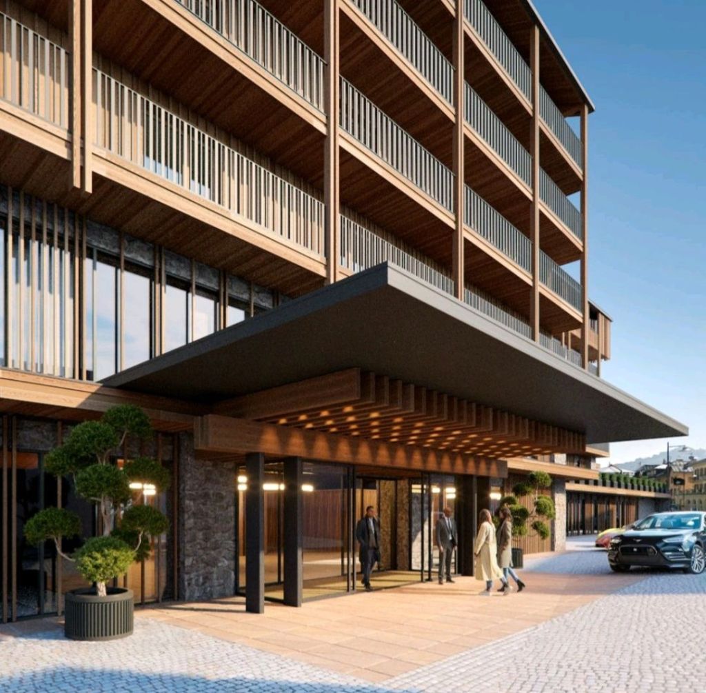 Exterior view of the Hotel Bellevue Cortina d'Ampezzo featuring a modern wooden facade, welcoming entrance, and lush landscaping, showcasing luxury alpine hospitality.