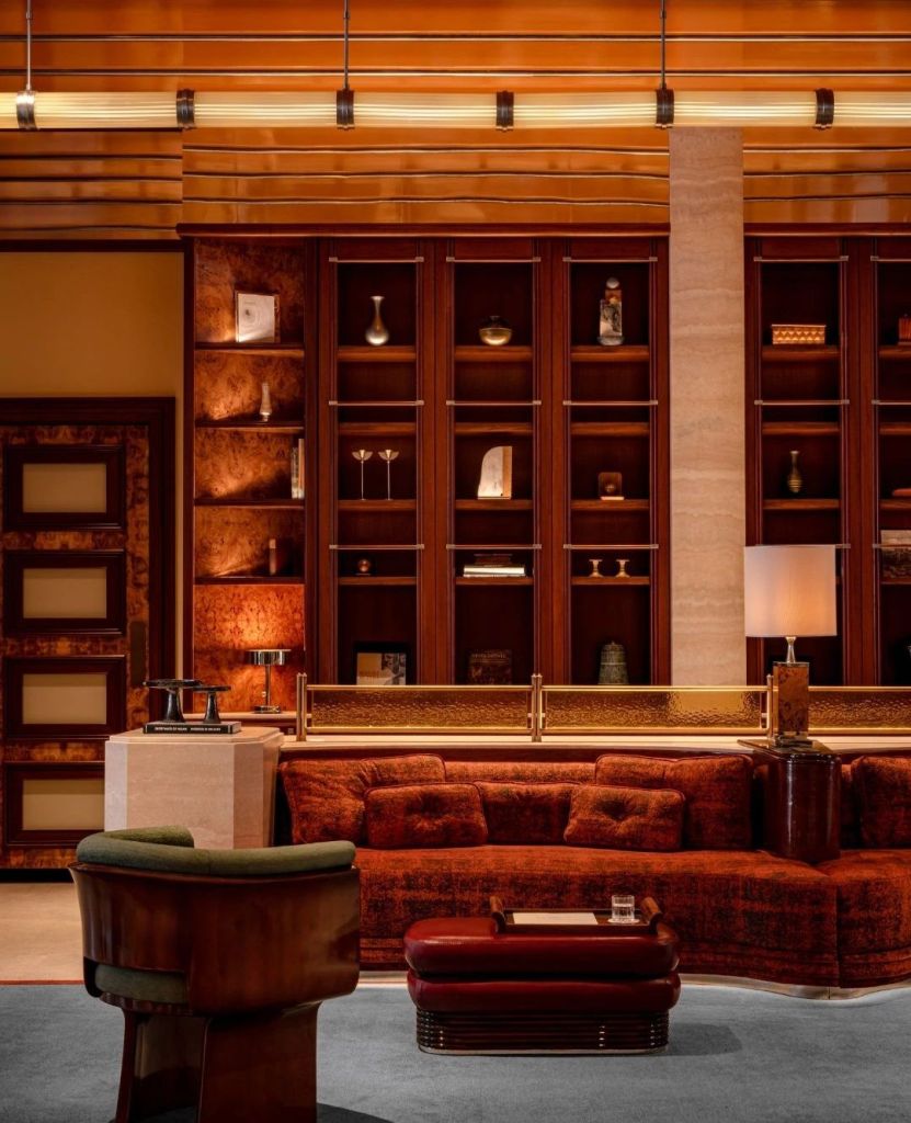 Interior view of a luxurious lounge area featuring a warm color palette, plush seating, and decorative shelves with various art pieces.