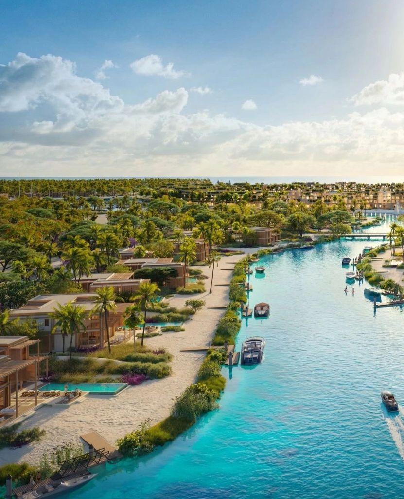 Aerial view of Laheq island featuring residential properties, lush greenery, sandy beaches, and a crystal-clear river with boats, showcasing a harmonious blend of nature and luxury living.