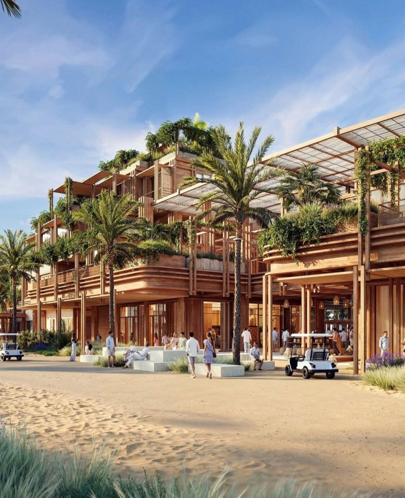 A modern wooden building surrounded by palm trees and sandy pathways, featuring open spaces with people enjoying the area, showcasing a resort-style living environment.