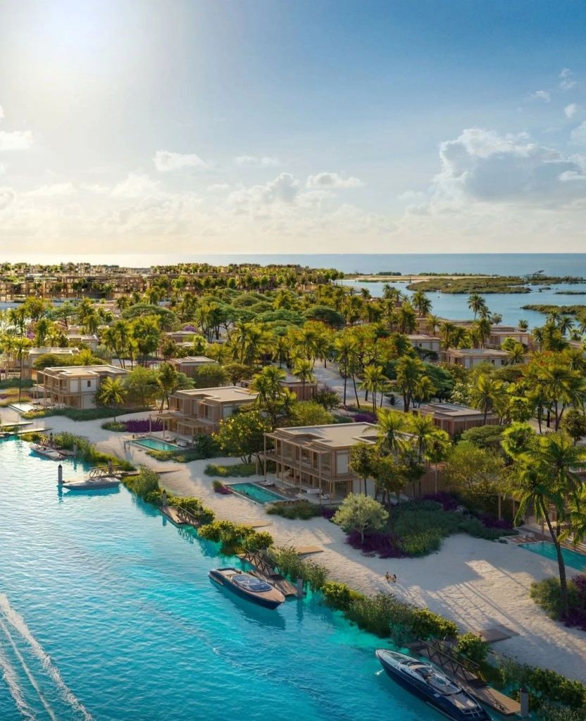 Aerial view of a luxurious beachfront resort development on Laheq Island, showcasing modern villas, lush palm trees, and turquoise waters, with yachts docked along a sandy shoreline.