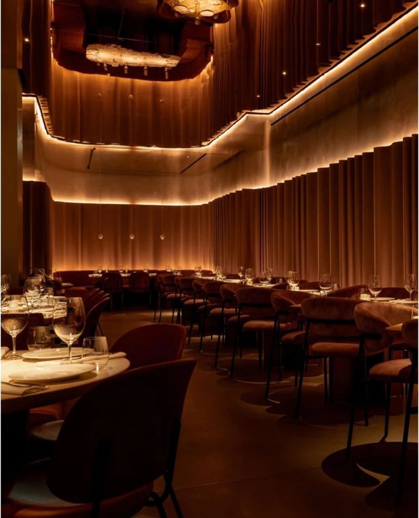 Interior of MR PORTER Steakhouse in London, showcasing a warm, ambient lighting design with stylish seating and elegantly set tables.