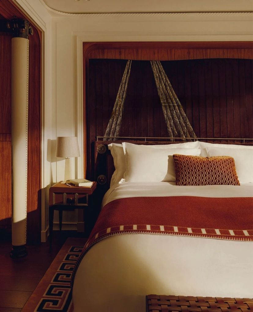 Luxurious suite interior of the Orient Express Corinthian, featuring a beautifully designed bed with elegant linens, a decorative pillow, and stylish bedside lighting.