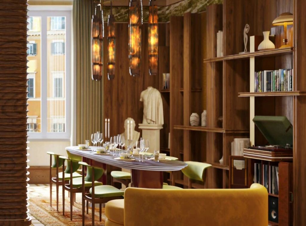An elegant dining area featuring a long table set for guests, surrounded by colorful chairs, with a wooden bookshelf and decorative objects in the background.