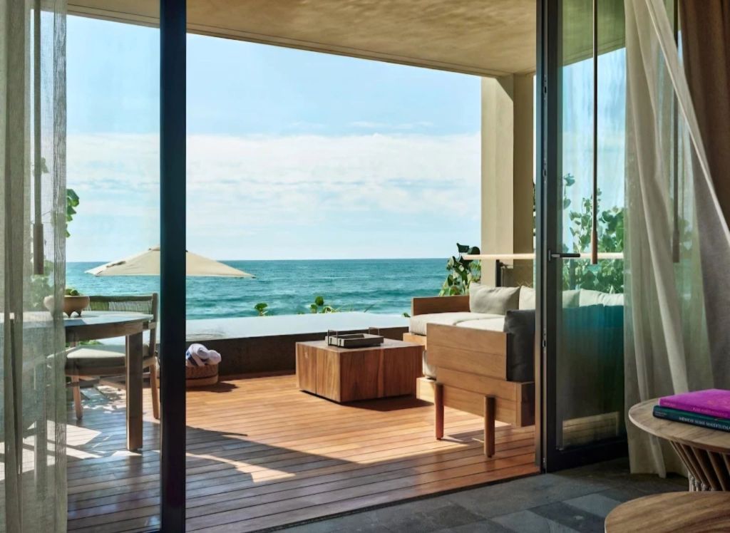View from a luxurious suite at Rosewood Mandarina, overlooking the ocean with a terrace featuring wooden furniture and a parasol.