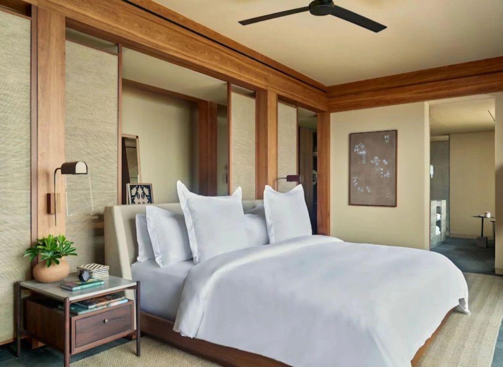 A luxurious bedroom in Rosewood Mandarina, featuring a king-size bed with white linens, wooden accents, and modern decor.