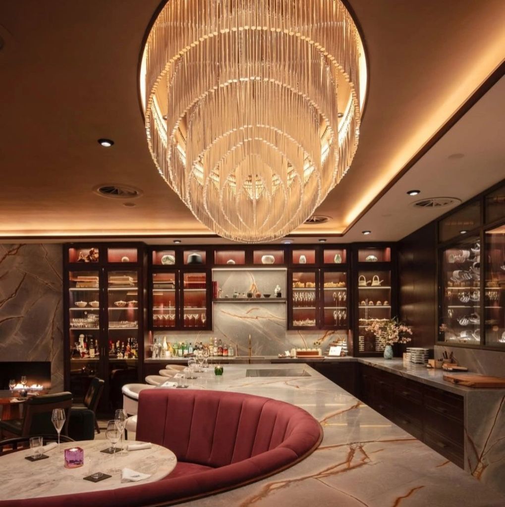 Interior of a modern dining space featuring an elegant chandelier, plush seating, and a marble dining table.
