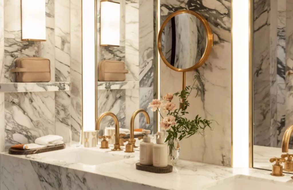 Elegant hotel bathroom featuring marble walls, stylish fixtures, and a modern round mirror, complemented by floral accents.