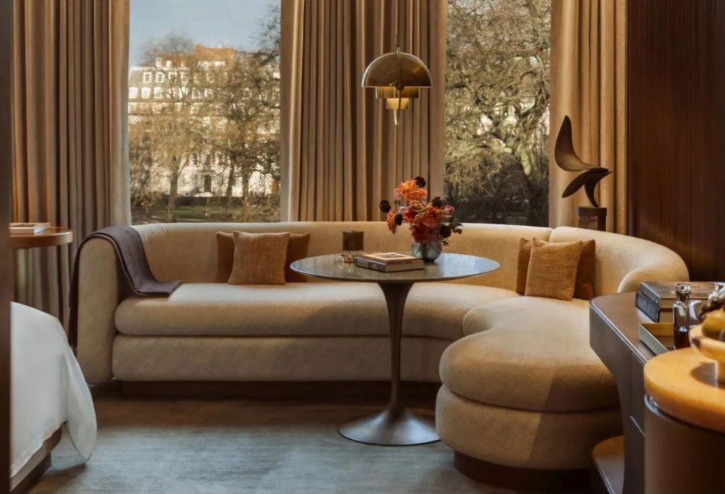 A luxurious suite at The Chancery Rosewood, featuring a comfortable curved sofa, elegantly arranged table with flowers, and large windows overlooking a scenic view.