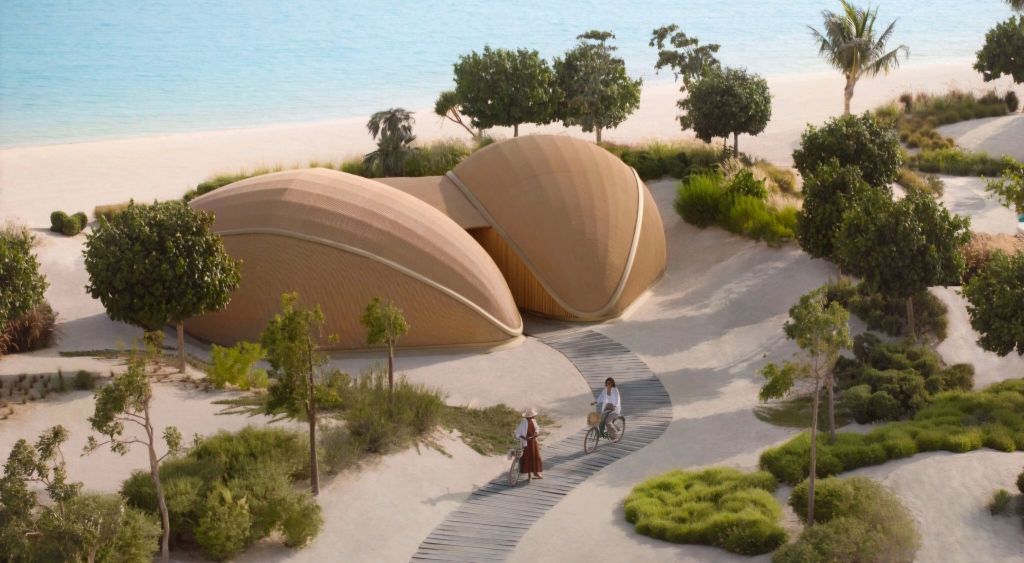 Aerial view of modern, shell-shaped residences nestled in a lush landscape near the beach, with people walking and cycling on a winding pathway.