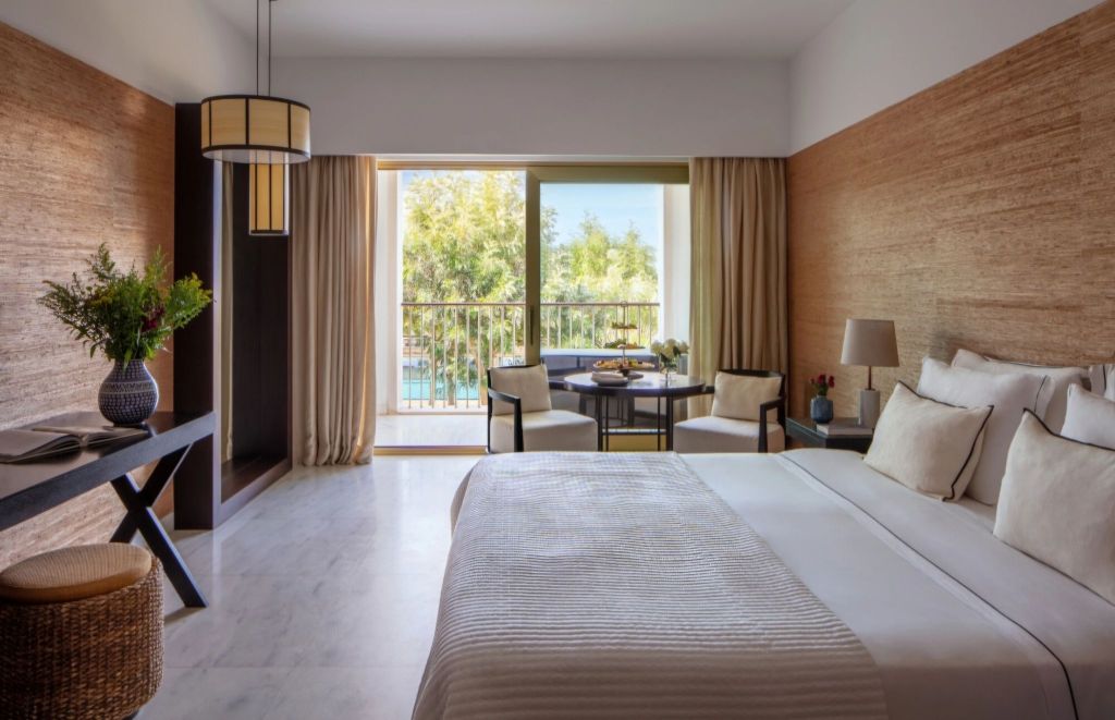 A luxurious hotel room featuring a plush bed, modern furnishings, a writing desk, and a balcony with scenic views of greenery.