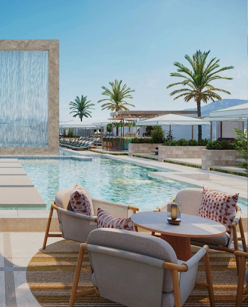 Luxurious seating area by a swimming pool adorned with a modern water feature and palm trees under a sunny sky.