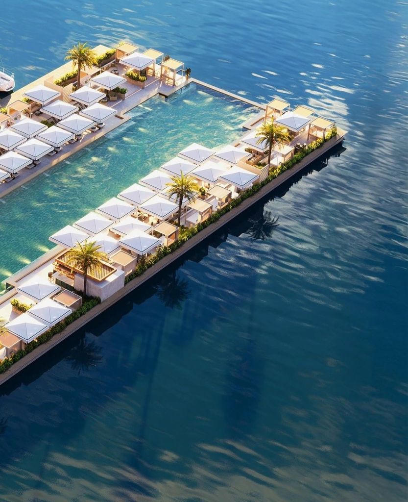 Aerial view of AURA Beach Montenegro showcasing luxurious beach cabanas and a swimming pool surrounded by palm trees, set against the tranquil Adriatic Sea.