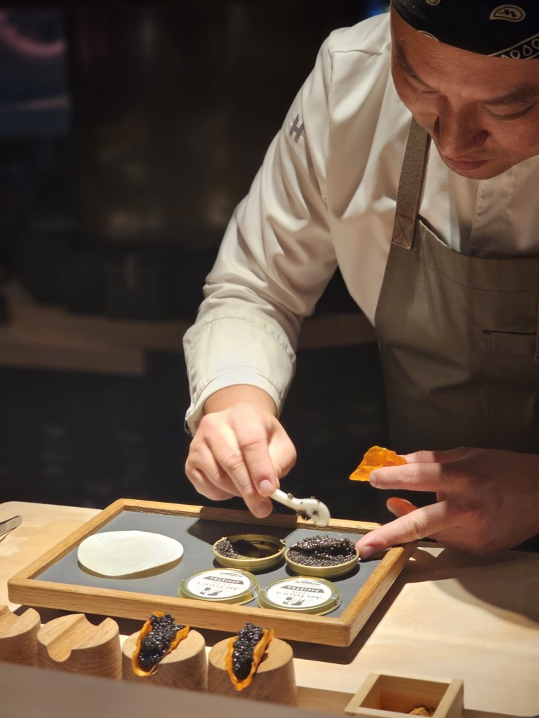 Chef preparing caviar and delicate ingredients at an intimate dining counter.