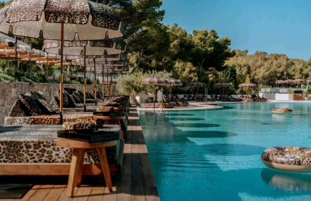 A luxurious pool area at CLAP HOUSE IBIZA featuring leopard print lounge chairs and umbrellas, set against lush greenery.