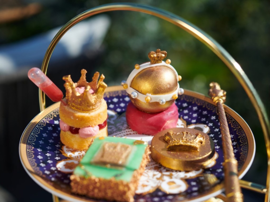 A beautifully arranged plate featuring intricate desserts inspired by royalty, including crown-shaped cakes, a golden orb, and a decorative wand, all presented on a patterned china plate.