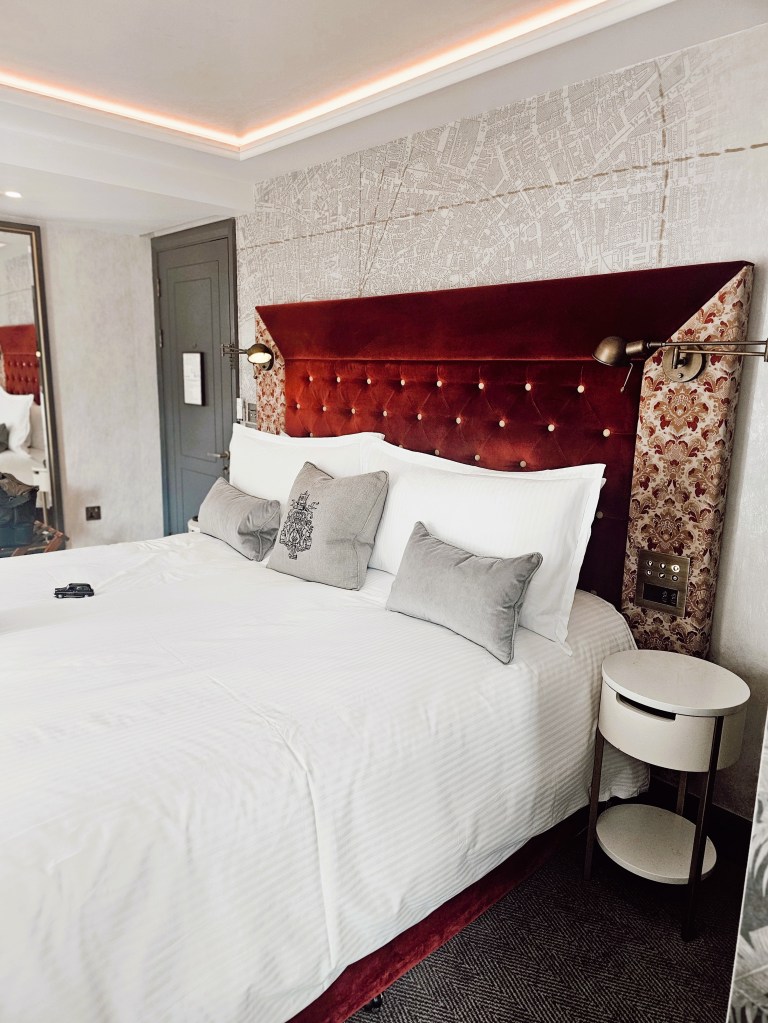 A beautifully designed hotel room featuring a velvet headboard, plush pillows, and stylish lighting, creating a warm and inviting atmosphere.