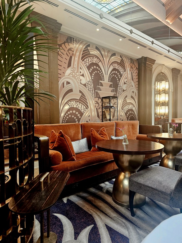 Luxurious seating area with an art deco inspired design in the Palm Court at Sheraton Grand London Park Lane, featuring plush orange upholstery, circular tables, and elegant décor.