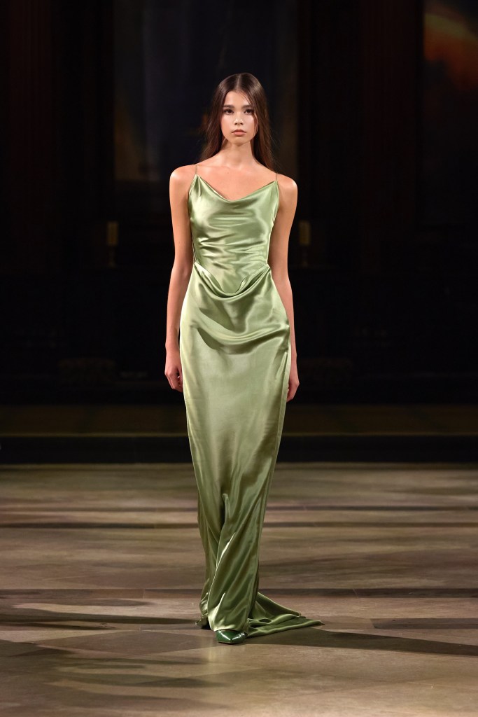 A model walks the runway wearing a smooth, green satin gown with delicate straps during a fashion show.