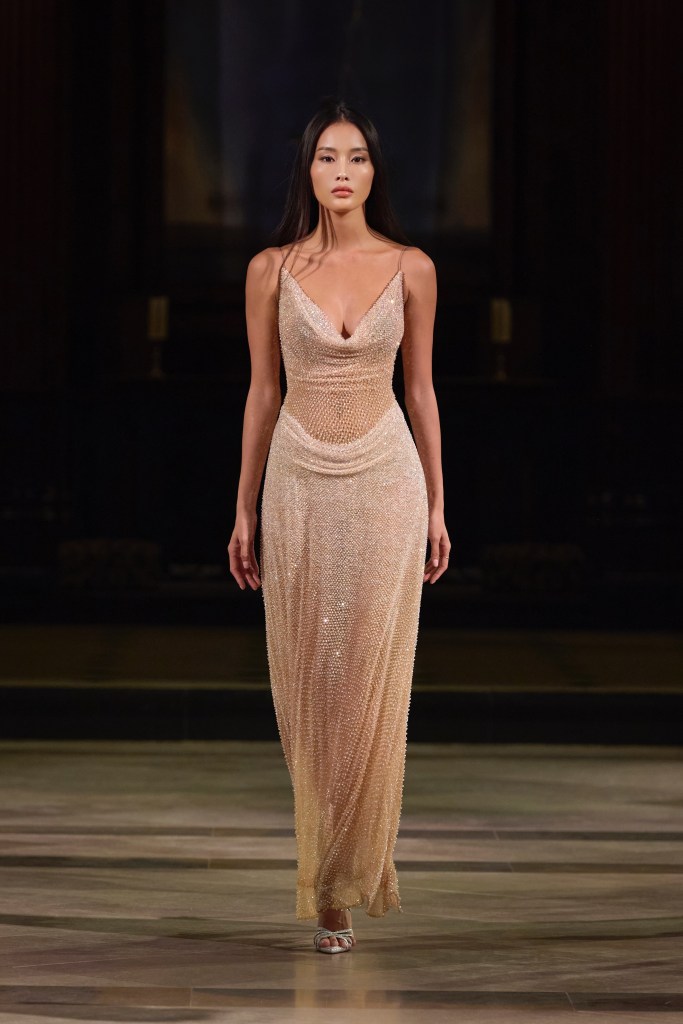 A model walks the runway wearing a shimmering, form-fitting gown adorned with intricate beadwork at London Fashion Week.