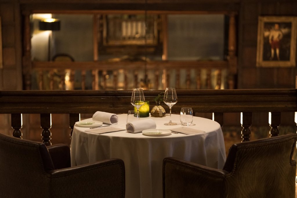 An elegant dining table set for two in Àclèaf restaurant at Boringdon Hall, featuring glasses, plates, and a candle, surrounded by a warm, subdued atmosphere and wooden detailing.