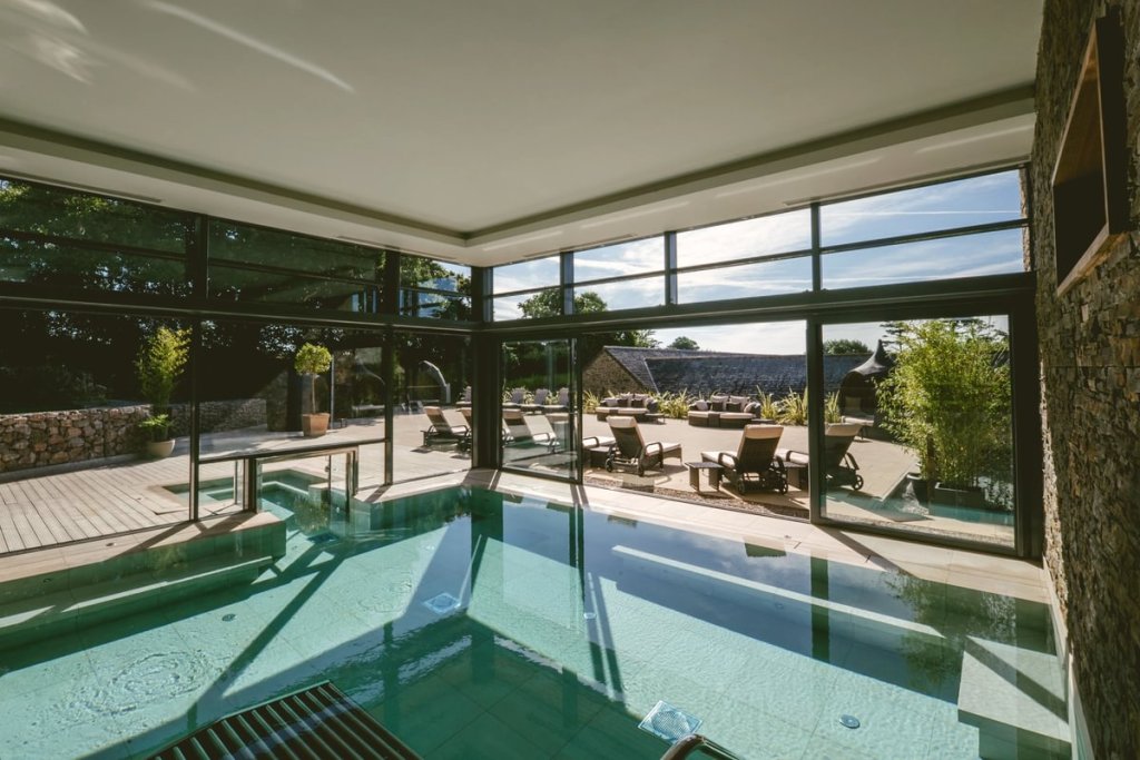 Interior view of the Gaia Spa at Boringdon Hall, featuring a serene indoor swimming pool with a view of an outdoor relaxation area surrounded by greenery.