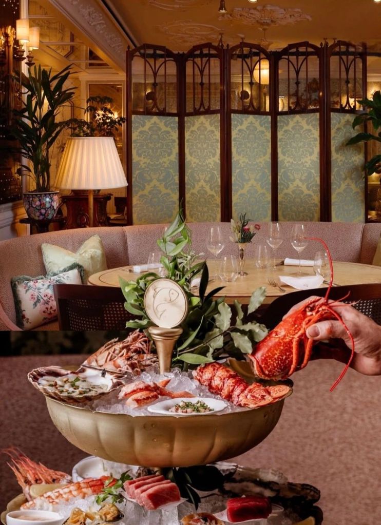 An elegant dining setting at Lilibet's Mayfair, featuring a lavish seafood platter with lobster and oysters in the foreground, and a cozy, well-decorated dining area with plush seating and intricate lighting in the background.