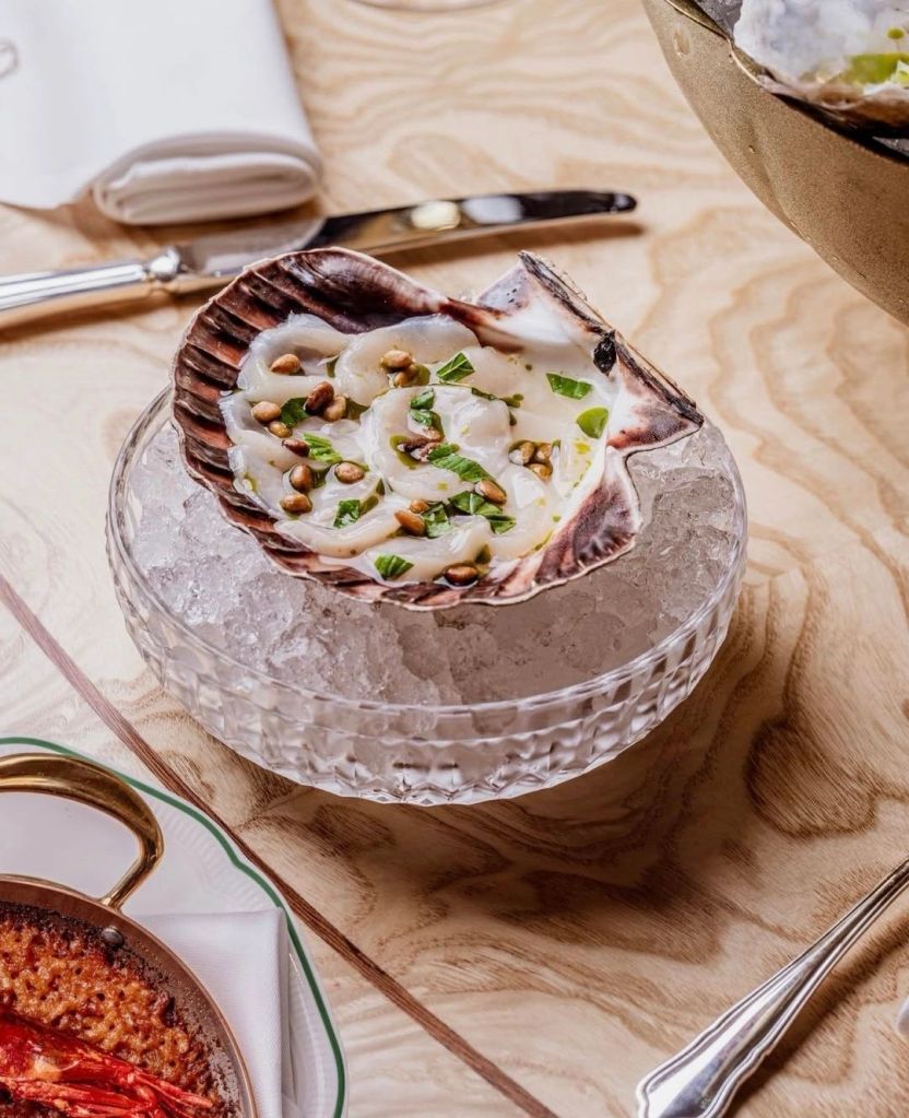 A beautifully presented dish featuring seafood in a shell, garnished with herbs and served on ice, set on an elegant wooden table.