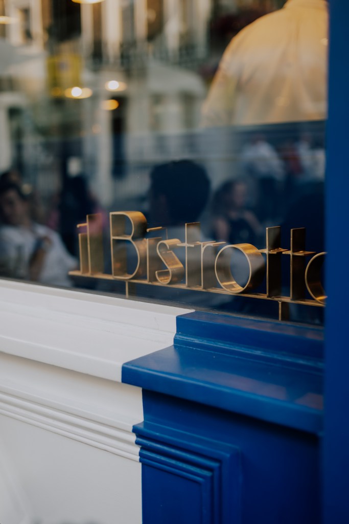 Close-up of the 'Il Bistrotto' sign reflecting the contemporary Mediterranean aesthetic against a backdrop of people dining.