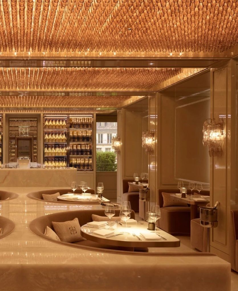 An elegantly designed restaurant interior featuring curved seating, stylish table settings, and a shimmering chandelier-like ceiling, with a view of the outside.