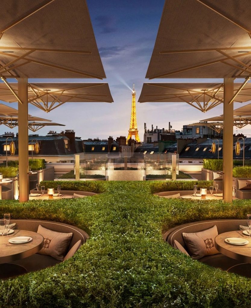 Rooftop dining area at RH Paris with lush greenery and views of the Eiffel Tower under a twilight sky.