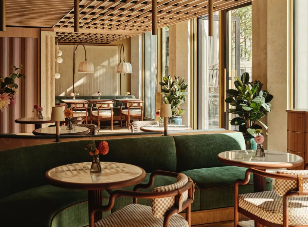 Interior view of a modern café at The Chancery Rosewood, featuring green seating, wooden tables, and decorative plants, with large windows allowing natural light.