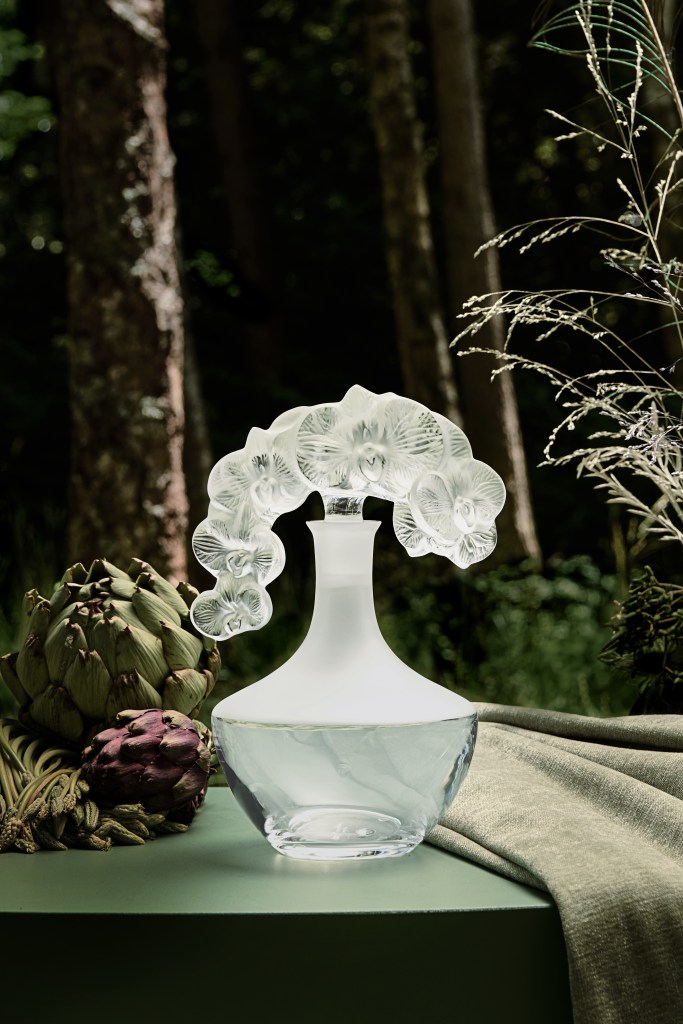 A beautifully crafted crystal vase inspired by nature, featuring a smooth base and an intricate floral design at the top, set against a serene forest backdrop.