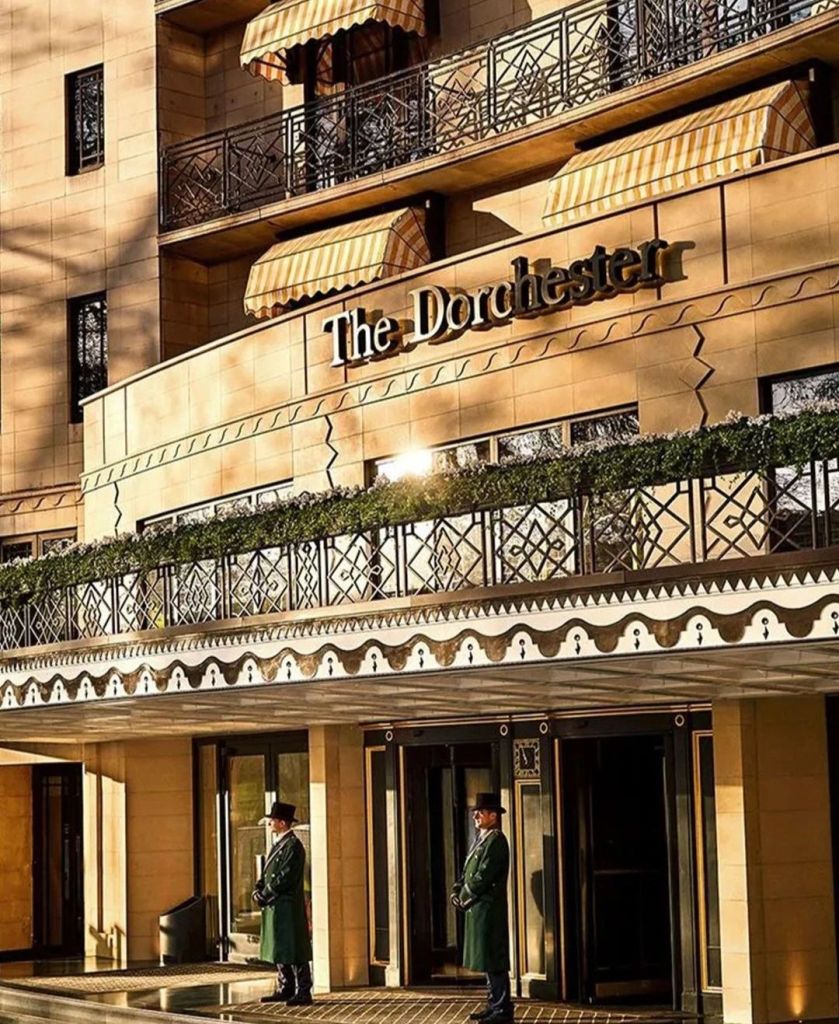 The entrance of The Dorchester hotel featuring its signature architecture, polished brass signage, and doormen in formal attire.
