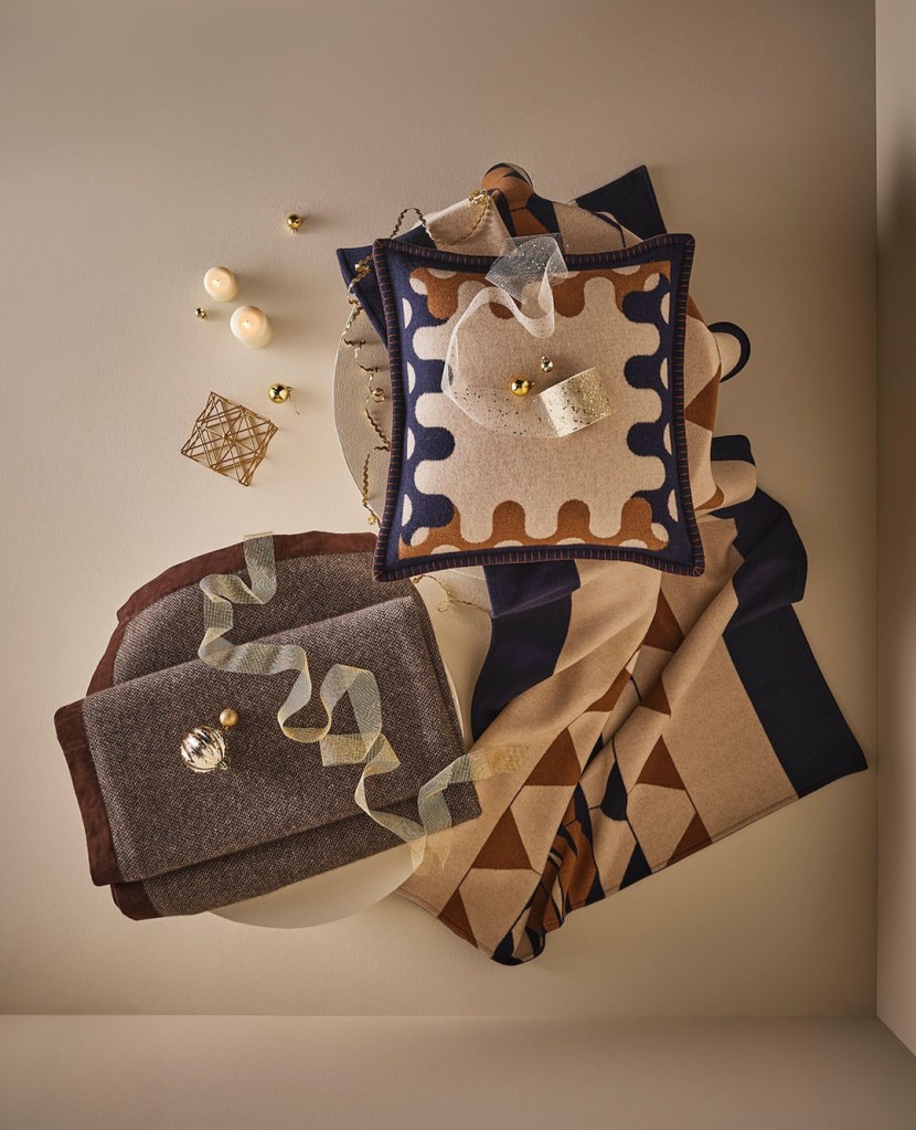 An overhead view of an arranged collection of luxurious textiles, including a patterned throw, embellished decorative pillows, and elegant wrapping ribbons, all set against a neutral background, evoking a sense of warmth and sophistication.