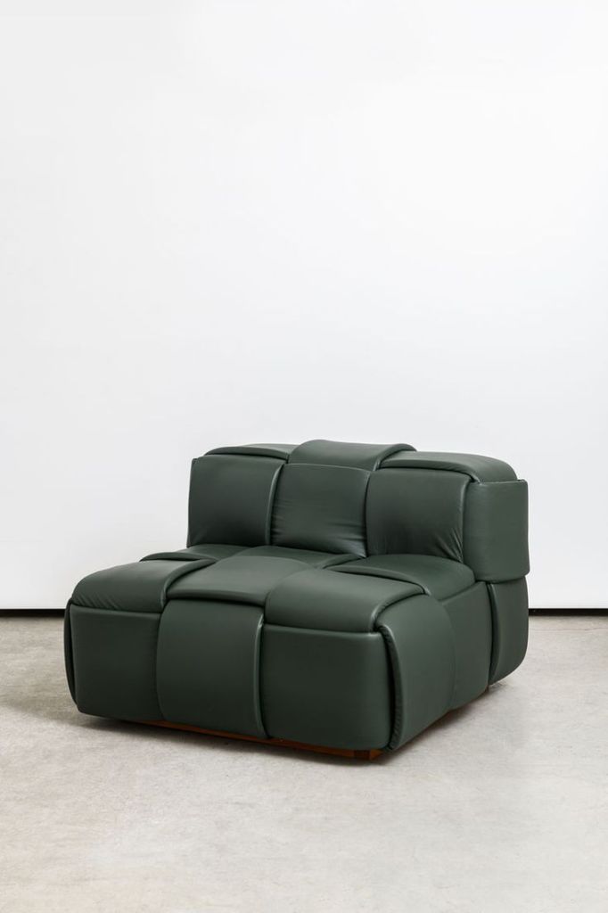 A contemporary green leather chair with a unique quilted design, set against a minimalist white background.