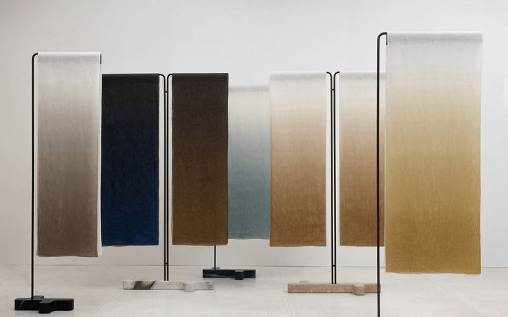 A display of colorful textile pieces arranged on stands, showcasing a gradient of hues from light to dark, with a modern and minimalistic aesthetic.