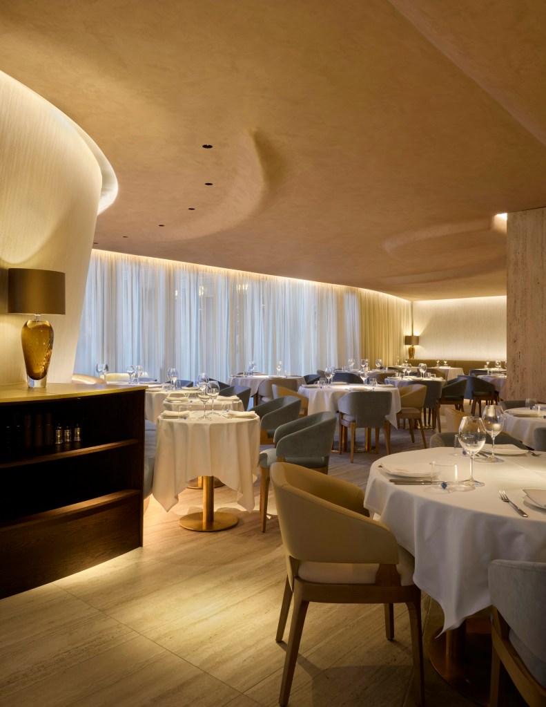 Interior of a stylish restaurant featuring elegantly set tables with white tablecloths, soft lighting, and modern decor.
