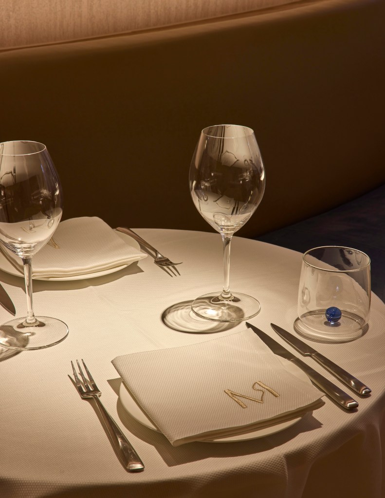 A elegantly set dining table featuring two wine glasses, neatly folded napkins, cutlery, and a decorative glass with a blue marble.