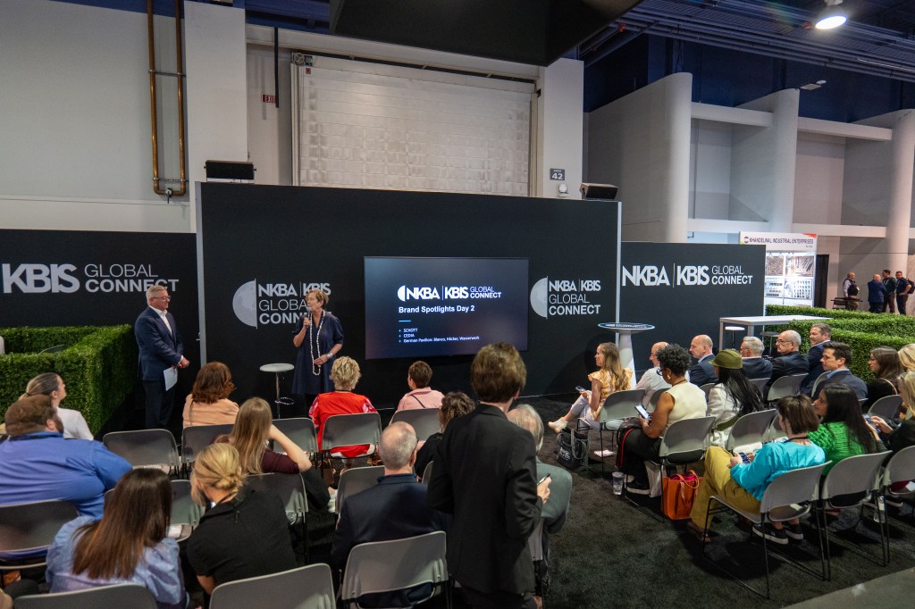 A presentation at the KBIS Global Connect event, featuring speakers discussing brand spotlights on stage, with an audience seated in front.