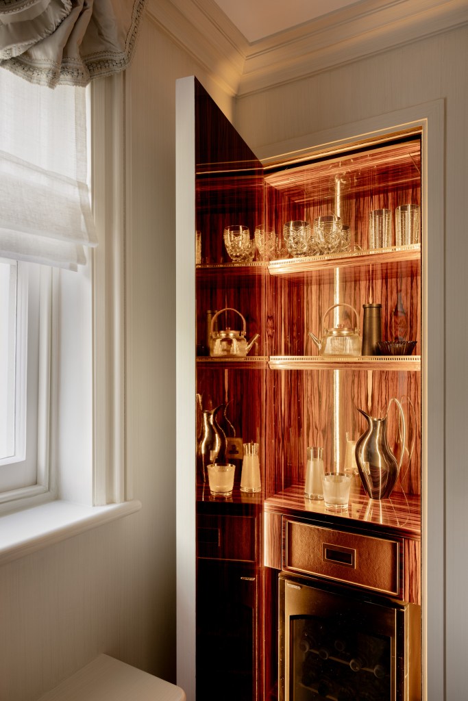 Stylish home bar cabinet with shelves displaying glassware and decorative items, illuminated from within, set within a finely crafted wooden frame.