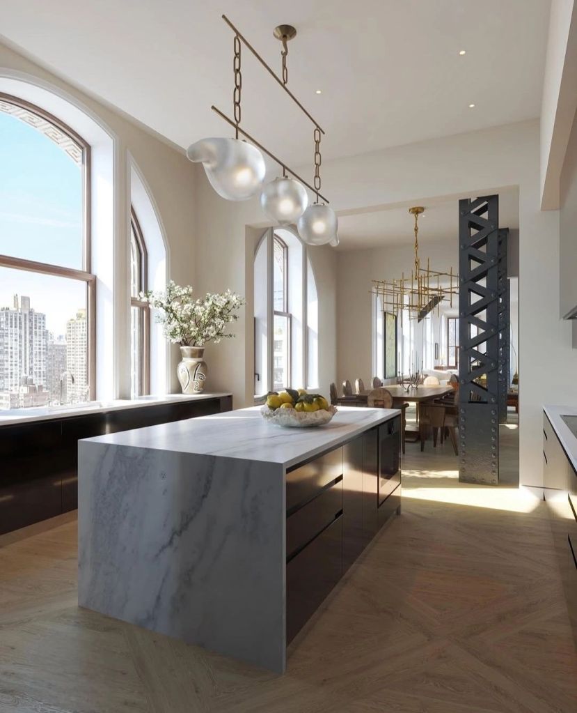 Modern kitchen featuring an island with a marble countertop, stylish pendant lighting, and large windows showcasing city views.