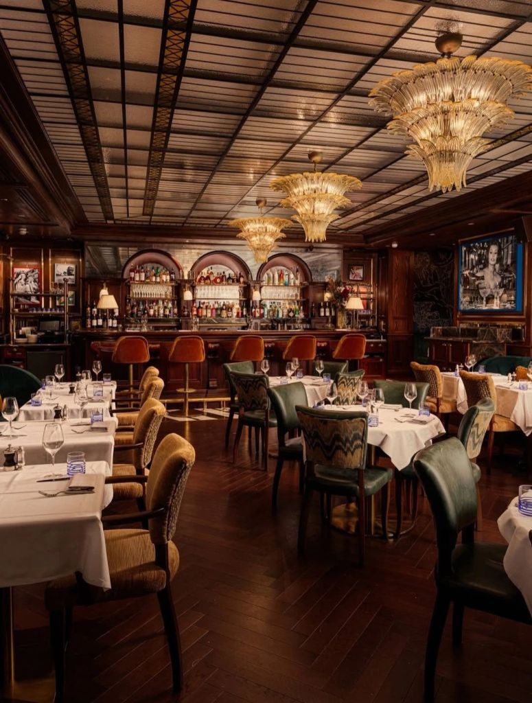 Elegant restaurant interior featuring wooden flooring, decorative chandeliers, and neatly arranged tables with white tablecloths.